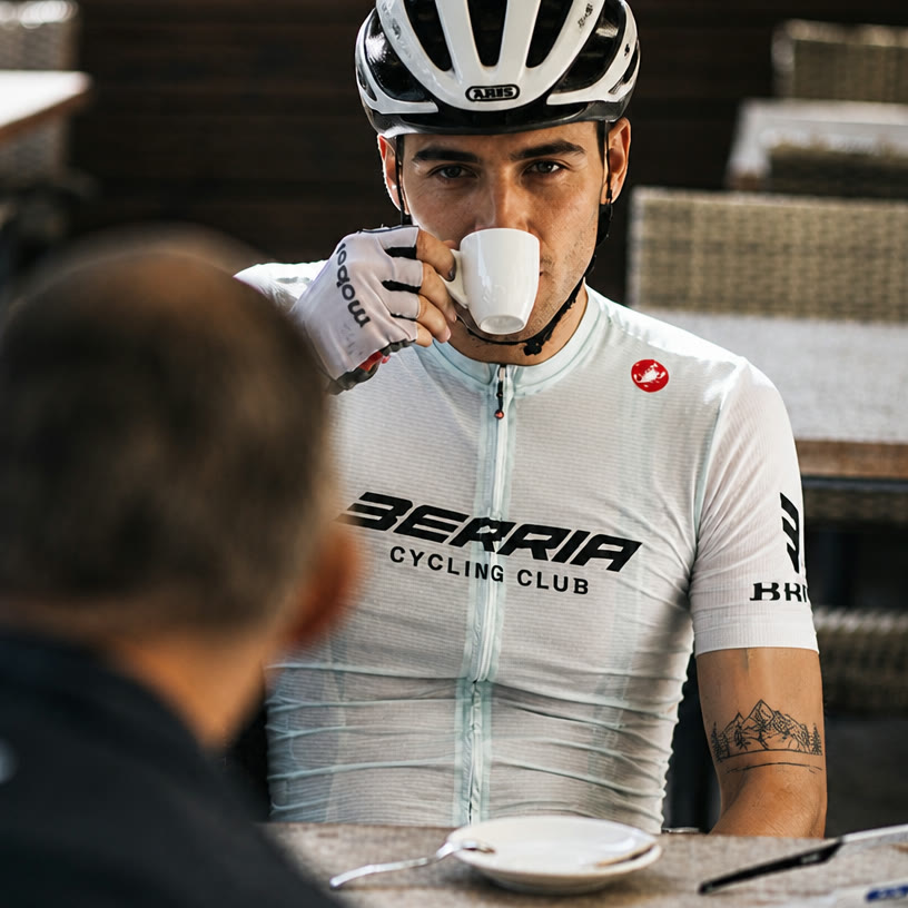 Ciclista con el maillot Berria Cycling Club tomando un café